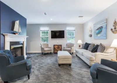 Nautical-themed sitting room with various seating options, blue accents, side tables, television, and carpeted floors