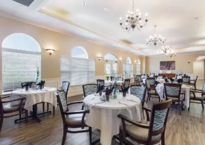 View of dining hall with table and chair sets, centerpieces, large windows, and chandeliers overhead