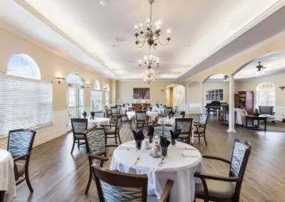 Large dining hall with table and chair sets, large windows, chandeliers overhead, and view of sitting area