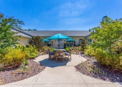 Path to outdoor dining table and chairs in courtyard surrounded by trees and garden area