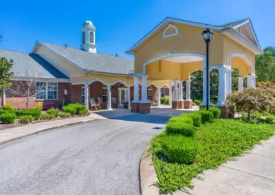 Main building exterior with large carport, lamp post, bushes and trees, and entrance road