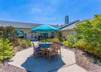 Outdoor dining area with table, chairs, umbrella, and various bushes, trees, and garden areas