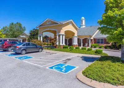 Handicapped parking area surrounded by bushes and grass in front of main building entrance and carport