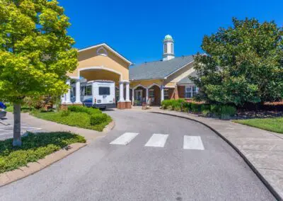 Road lined with trees and shrubbery leading to front entrance with community shuttle in view under carport